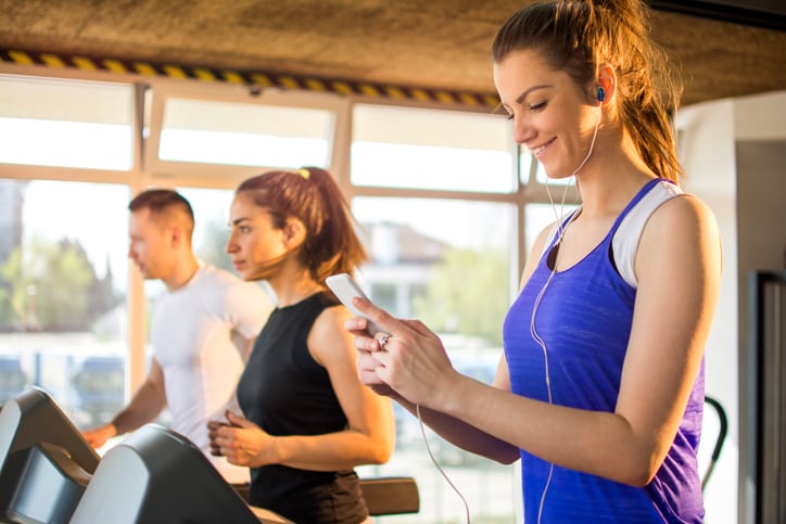 Young woman excited to watch Netflix on her phone on the treadmill.